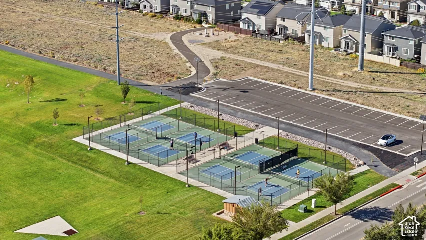 Multiple pickleball courts, paved parking area, extensive green space, adjacent paved pathway, and residential structures in the background