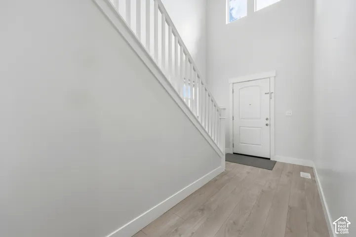 Vaulted ceiling entry with transom windows, wood-finish flooring, and a staircase featuring a white railing