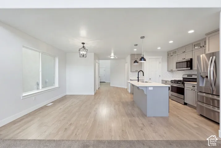 Open-concept living space featuring wood-finish flooring, a kitchen island with pendant lighting, stainless steel appliances, and white subway tile backsplash