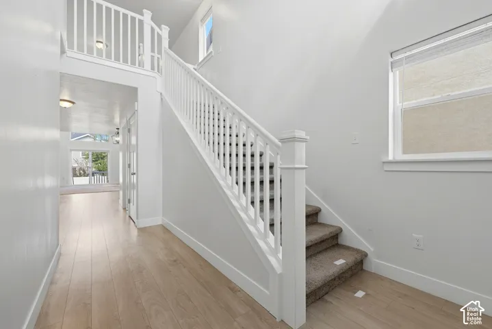 Light wood-finish flooring, white walls, carpeted staircase, white railing, and an upper-level window