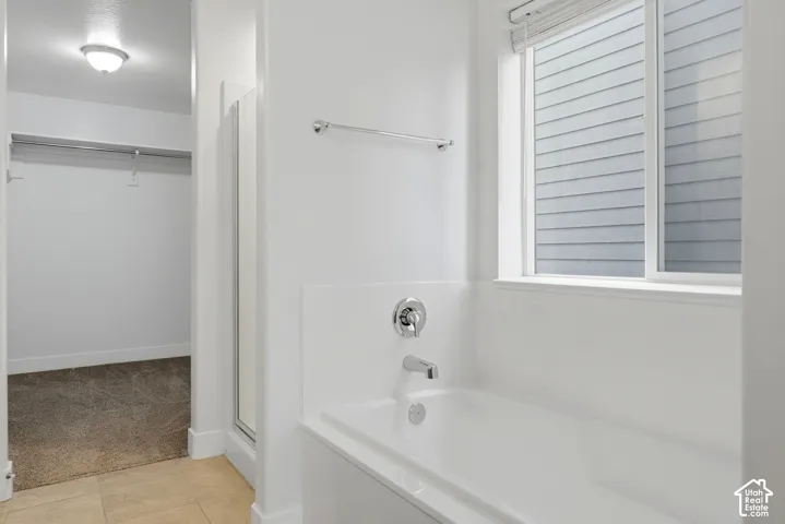 White bathtub with chrome fixtures, window with blinds, and tile flooring