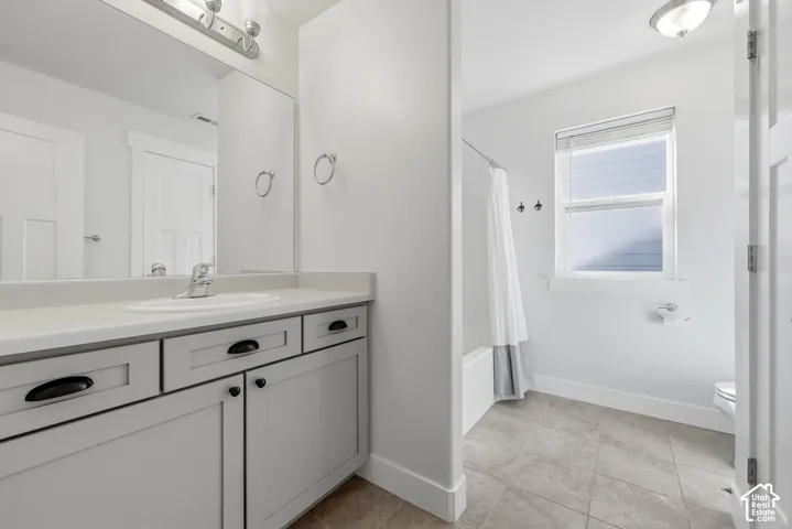 Bathroom featuring a single vanity, undermount sink, ample storage cabinetry with dark hardware, a bathtub with an overhead shower, and a window with blinds