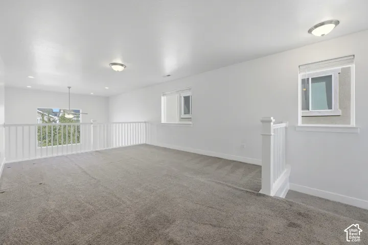 Carpeted loft space with white painted walls, white railing, recessed lighting, and windows with blinds