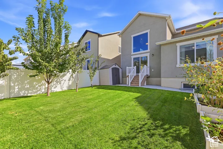 Expansive green lawn, elevated deck with white railing, large sliding glass door, prominent upper-level window, and a storage shed