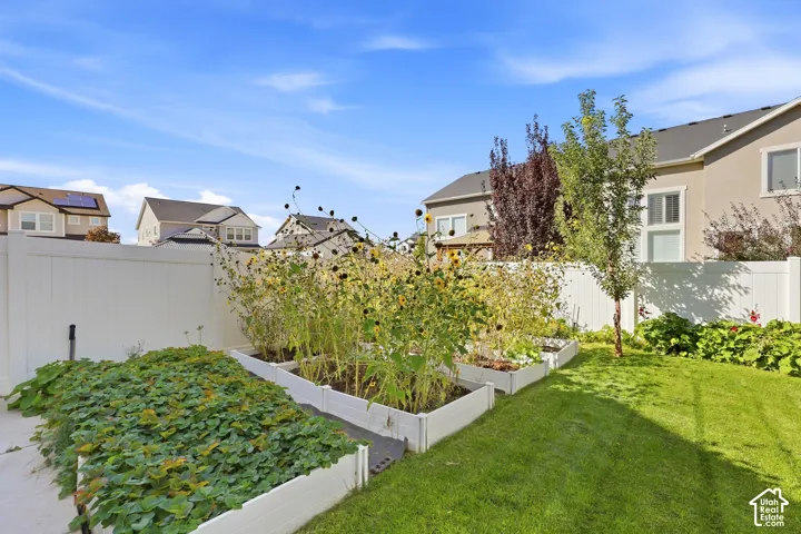 Landscaped backyard featuring a manicured lawn, white vinyl fencing, and multiple raised garden beds