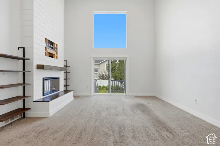 Spacious living area featuring a tall ceiling, a prominent fireplace with a wood-finish mantel, built-in shelving, and a large window