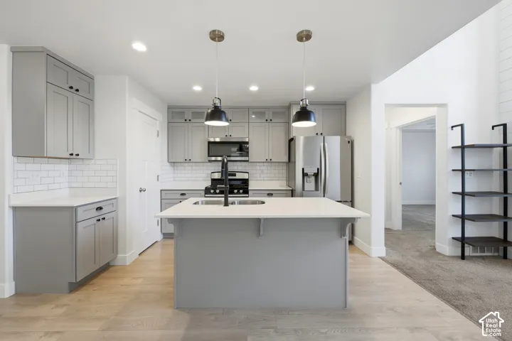 Kitchen featuring a central island, grey cabinetry, white subway tile backsplash, stainless steel appliances, and wood-finish flooring