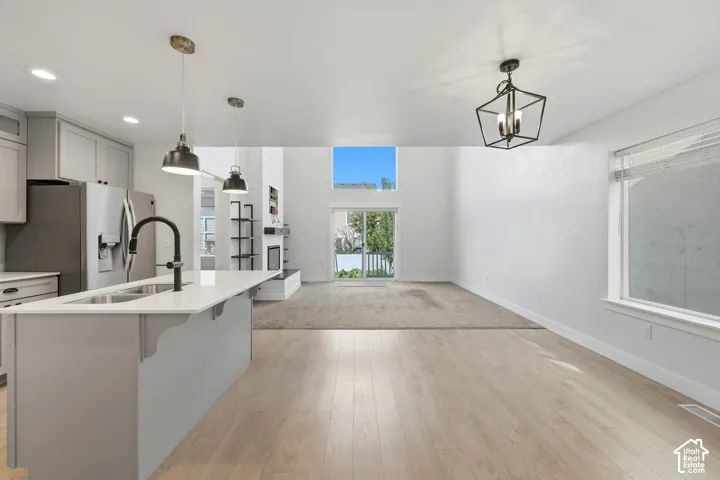 Open-concept living space featuring wood-finish flooring, a kitchen island with sink, contemporary pendant lighting, a vaulted ceiling, and a sliding glass door