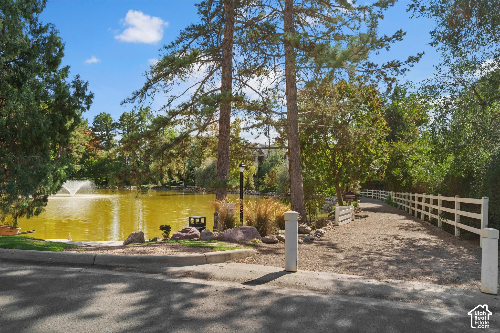Water feature with fountain, mature trees, white picket fencing, and a gravel pathway