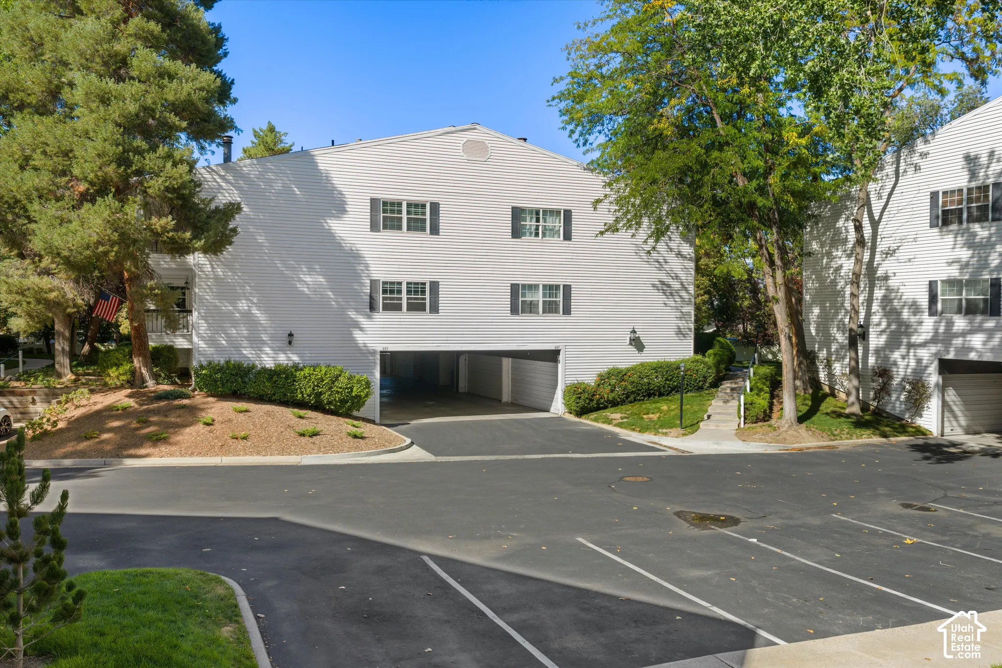 White siding exterior featuring black window shutters, a covered parking area, and mature trees