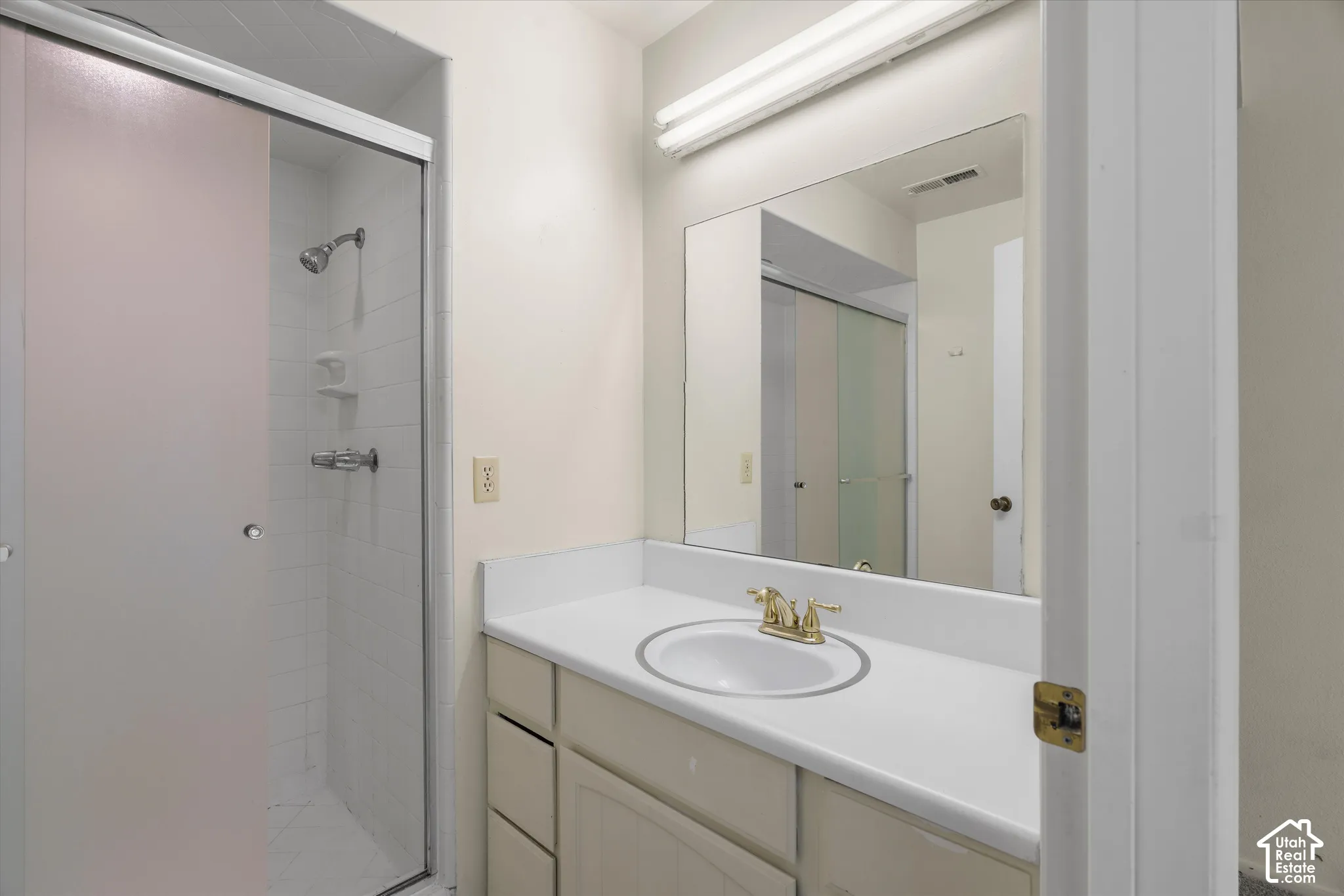 Vanity with an integrated sink and brass-finish faucet, framed mirror, and a shower with a clear glass enclosure