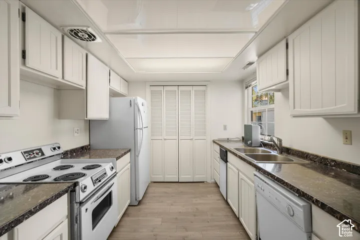 Galley kitchen featuring white cabinetry, stone-look countertops, wood-finish flooring, a double basin sink, and white appliances
