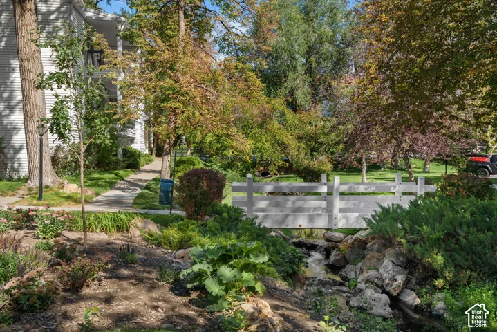White painted pedestrian bridge spanning a natural rock stream, surrounded by lush landscaping and mature trees