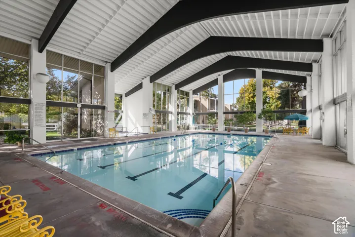 Indoor swimming pool with lane markers, enclosed by full-height windows, featuring a sloped white ceiling with exposed dark beams