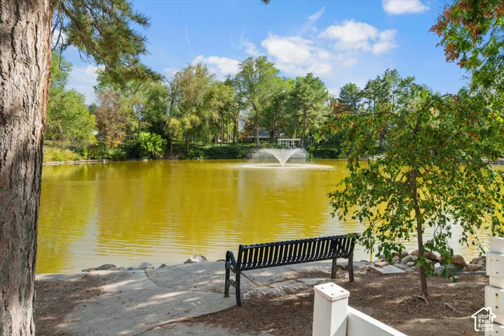 Lakeside setting featuring a water fountain, mature trees, and a paved pathway