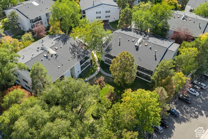 Multiple residential buildings featuring balconies, surrounded by mature trees, with adjacent paved parking