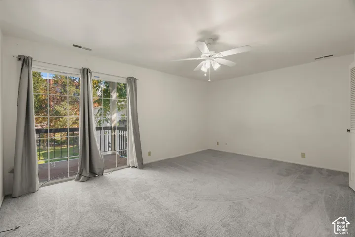 Carpeted room with a ceiling fan, featuring sliding glass doors opening to a balcony with black railings