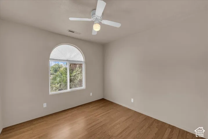 Arched window with pleated shade, wood-finish flooring, and ceiling fan with integrated lighting