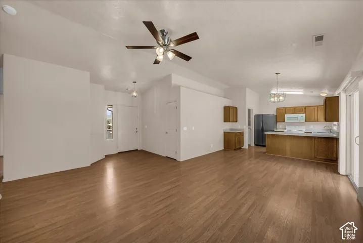Spacious interior featuring wood-finish flooring, a kitchen with wood cabinetry, white countertops, and a full suite of appliances, and a ceiling fan with integrated lighting
