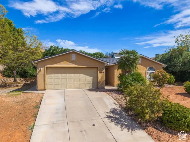 Stucco exterior with an attached garage, arched window, and mature landscaping