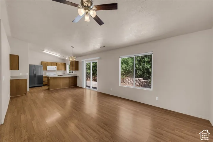 Vaulted ceilings, wood-finish flooring, kitchen island with seating, stainless steel refrigerator, and glass sliding door
