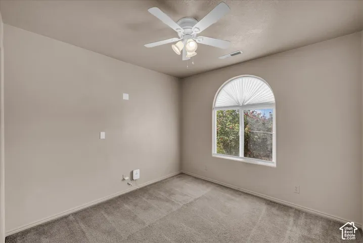 Arched window with pleated shade, textured carpeting, ceiling fan with integrated lighting, and neutral wall paint