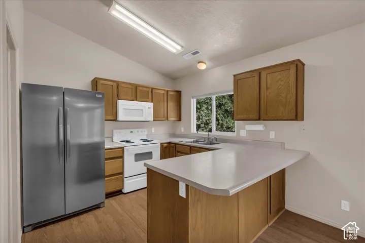 Kitchen featuring wood cabinetry, light-toned countertops, a stainless steel refrigerator, white appliances, and wood-finish flooring