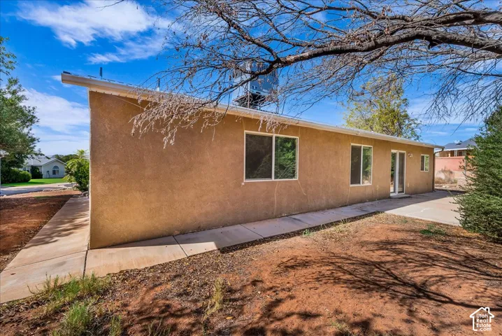 Stucco exterior featuring multiple windows and sliding glass doors, concrete patio, and a concrete pathway