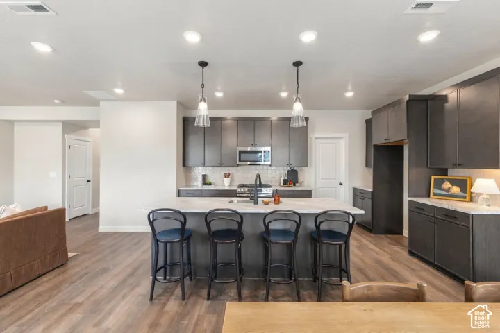 Kitchen featuring dark wood-finish cabinetry, stainless steel appliances, a tile backsplash, light-toned countertops, and wood-finish flooring