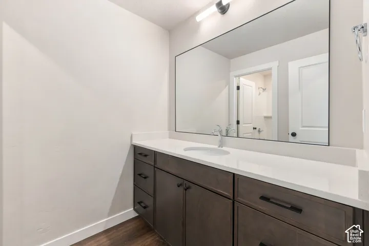 White countertop with an integrated sink, dark wood-finish vanity cabinetry, contemporary black hardware, and an expansive wall-mounted mirror