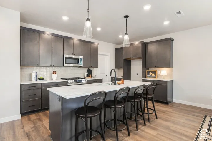 Modern kitchen featuring gray cabinetry, stainless steel appliances, a tile backsplash, and an island with seating