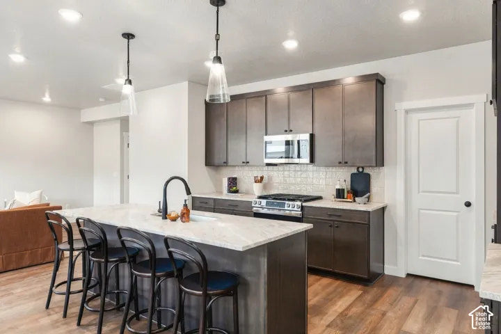 Spacious kitchen featuring an island with seating, stainless steel appliances, wood-finish flooring, and pendant lighting