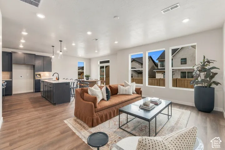 Open-concept living area with wood-finish flooring, a kitchen island with seating, dark-toned cabinetry, and recessed lighting