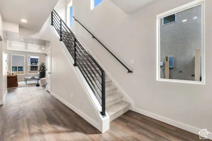 Wood-finish flooring, staircase with metal railing, carpeted treads, recessed lighting, and a white window frame