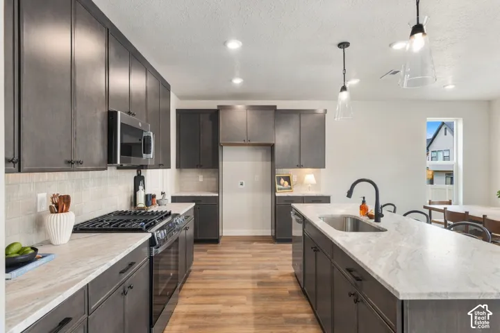 Modern kitchen featuring wood-finish flooring, dark cabinetry, light-toned countertops, a stainless steel gas range, and a kitchen island with an undermount sink