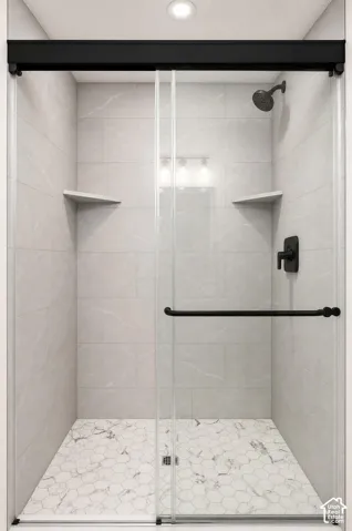 Walk-in shower with clear glass enclosure and black hardware, featuring a hexagonal tile floor, tiled walls, and two built-in corner shelves