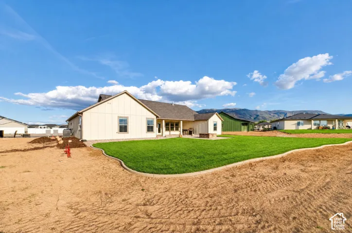 Expansive rear yard featuring a manicured lawn, concrete patio, and mountain backdrop