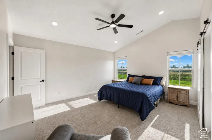 Spacious primary bedroom featuring vaulted ceilings with recessed lighting and a ceiling fan, abundant natural light from dual windows overlooking pastoral grounds, neutral wall finishes, and wood-finish nightstands with storage drawers