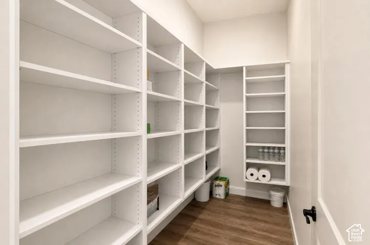 Spacious walk-in closet featuring extensive white shelving with adjustable shelves throughout, wood-finish flooring, and ample storage capacity for organized wardrobe and household items