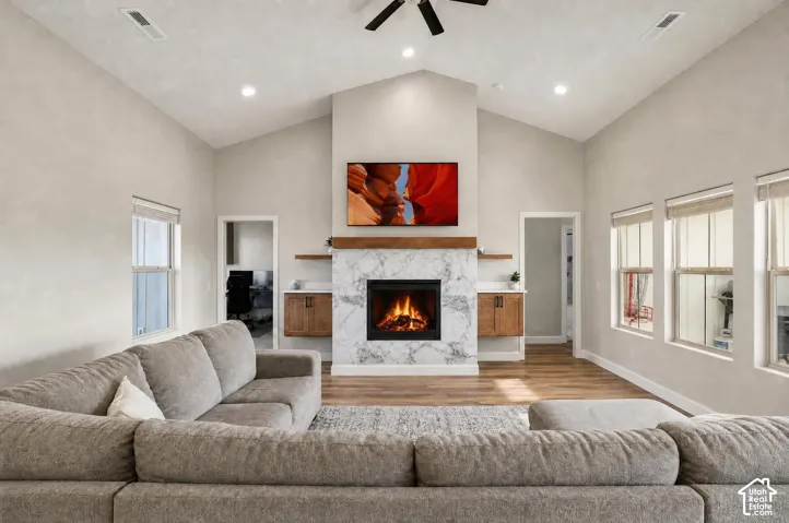 Vaulted ceilings with recessed lighting, a fireplace with marble-look surround, a wood mantle, built-in cabinetry, and wood-finish flooring