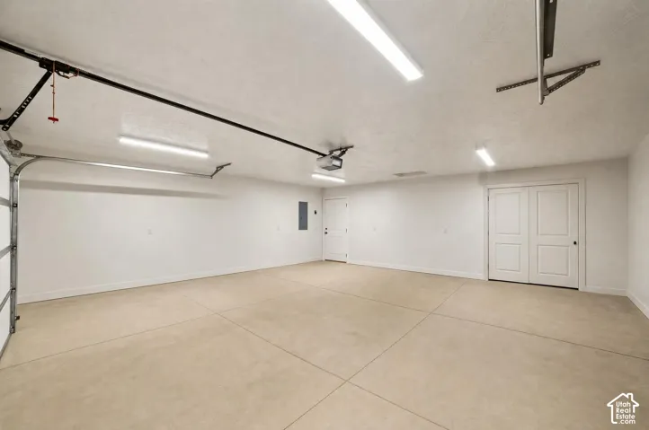 Spacious garage with light-colored concrete flooring, multiple overhead fluorescent light fixtures, an exterior access door, and double interior doors