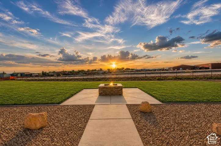 Expansive backyard featuring a central fire pit, concrete patio, and a combination of manicured lawn and decorative gravel