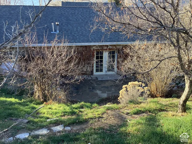 Stone veneer exterior with a patio, double French doors, and mature landscaping