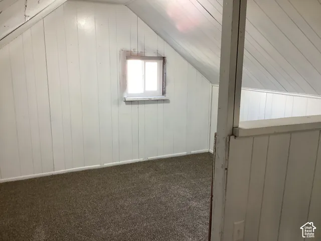 Sloped ceiling with painted paneling, wall-mounted window, and carpeted flooring. Loft bedroom with a closet.