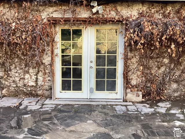 Stone exterior wall with climbing vines, multi-pane glass doors, and a stone patio