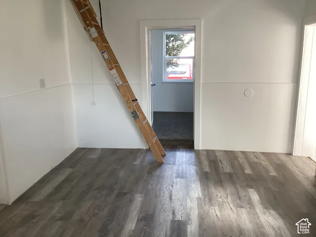 Wood-finish flooring, white paneled walls, and a doorway to an additional room. West bedroom, kitchen, and latter for loft bedroom.