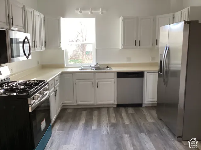 Kitchen featuring white cabinetry, stainless steel appliances, wood-finish flooring, light-toned countertops, and a window above the sink