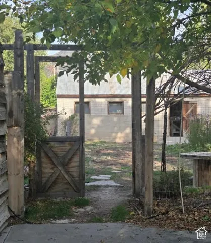 Wooden fence with an open gate, a stone pathway, and a detached structure and a detached brick shop