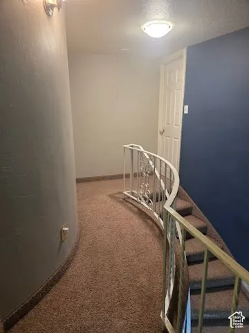 Curved hallway with carpet flooring and a decorative metal railing leading to a staircase