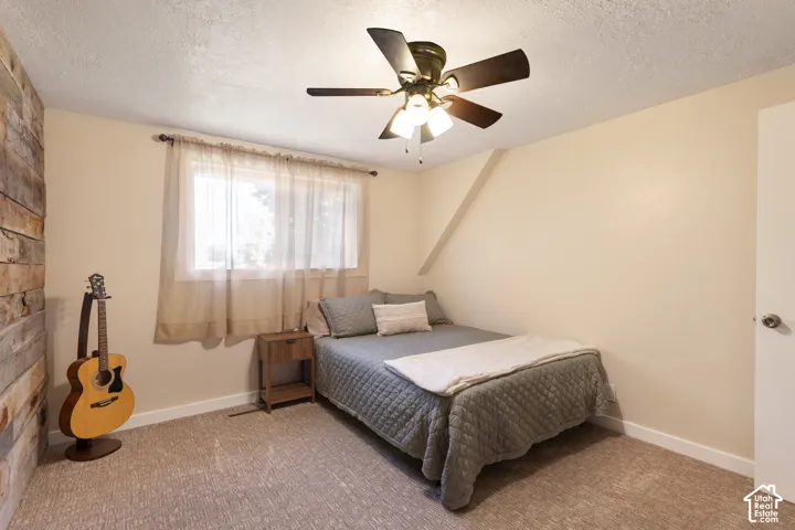 Textured accent wall, ceiling fan with integrated lighting, window with ample natural light, neutral wall colors, and carpet flooring
